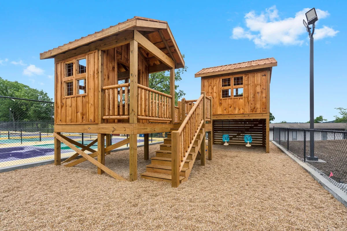 A playful exterior scene featuring a children’s playhouse, slide, swing set, and sandbox. Kids are engaged in imaginative play, while the space also hints at family gatherings and community events. The overall mood is joyful and vibrant, reflecting shared adventures and childhood excitement.