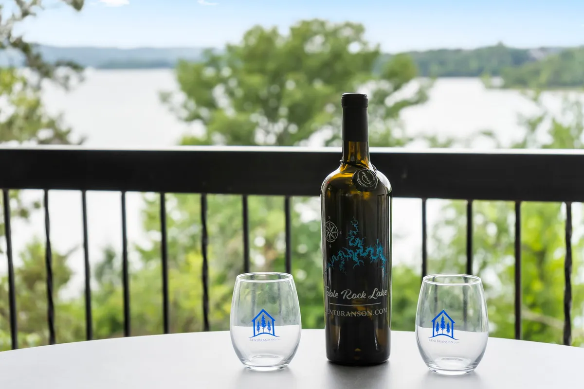 An exterior scene showing a private deck with a wine bottle and two glasses, set against a tranquil lake view. The scene captures a sense of peaceful relaxation and connection to the outdoors, with the deck positioned to maximize enjoyment of the scenery.