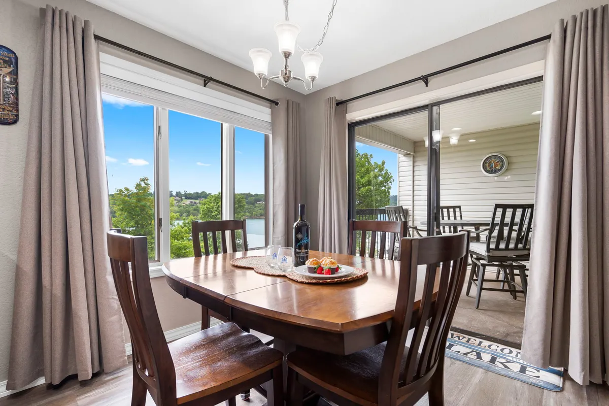 A warm and welcoming dining area adjacent to large windows, providing views of the outdoors and plenty of natural light. The dining table is ready for family meals or entertaining guests, and the chandelier adds a touch of elegance to the inviting setting.