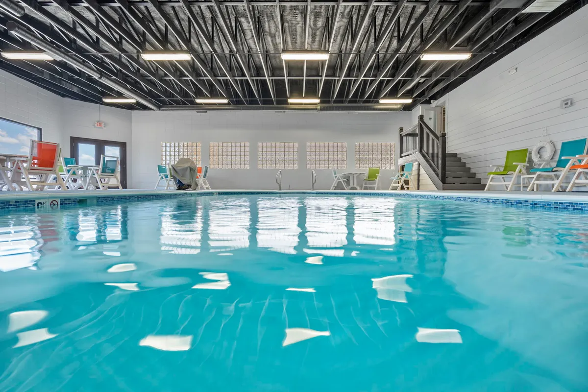This image features the indoor swimming pool filled with natural light from large windows. Colorful lounge chairs surround the pool, creating a cheerful and welcoming atmosphere perfect for families and groups regardless of the weather.
