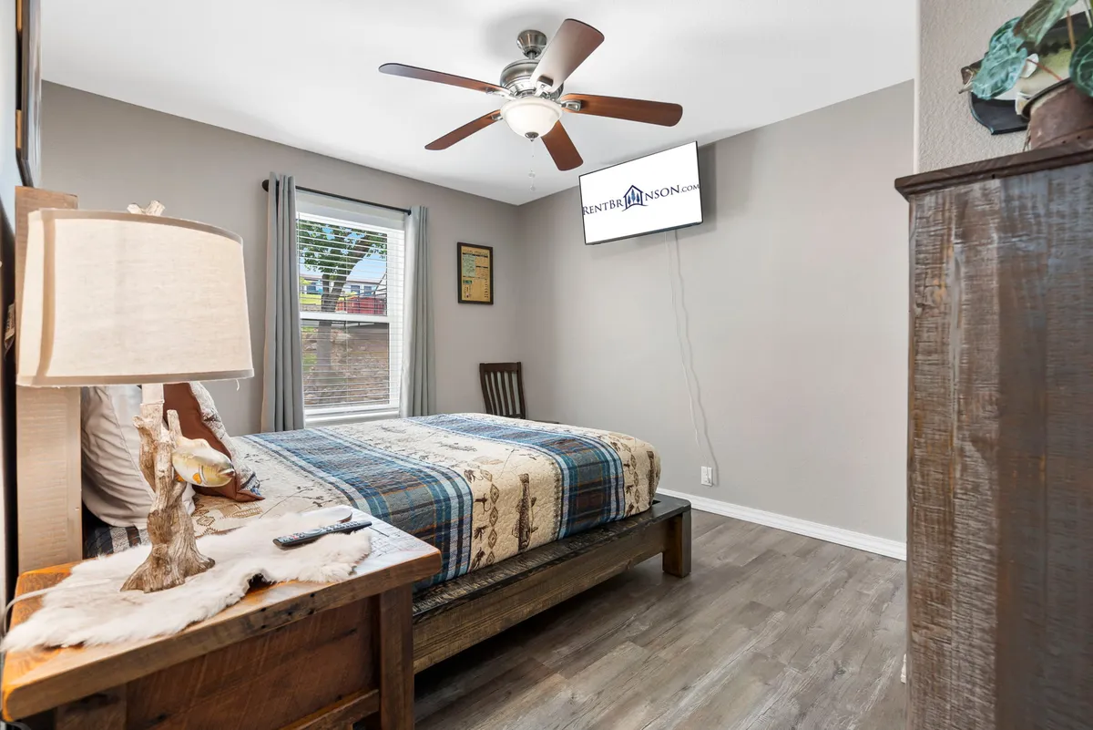 A bright, inviting bedroom with a comfortable bed, nightstand, window bringing in natural light, and a wall-mounted TV. The space feels serene and perfectly suited for restful sleep or catching up on favorite shows.