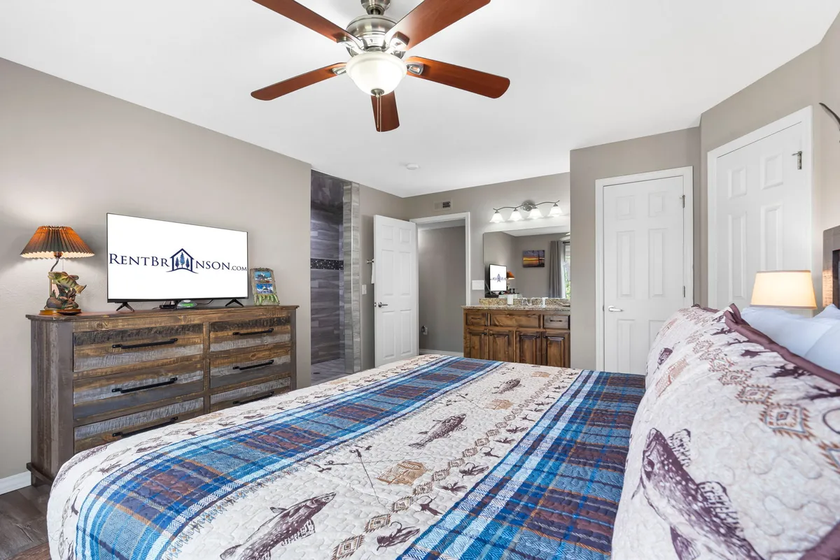 A cozy bedroom featuring a bed with a patterned blanket, a wooden dresser, and a television set atop. The warm lighting and neatly arranged furniture create a welcoming space perfect for relaxing and watching TV after a long day.