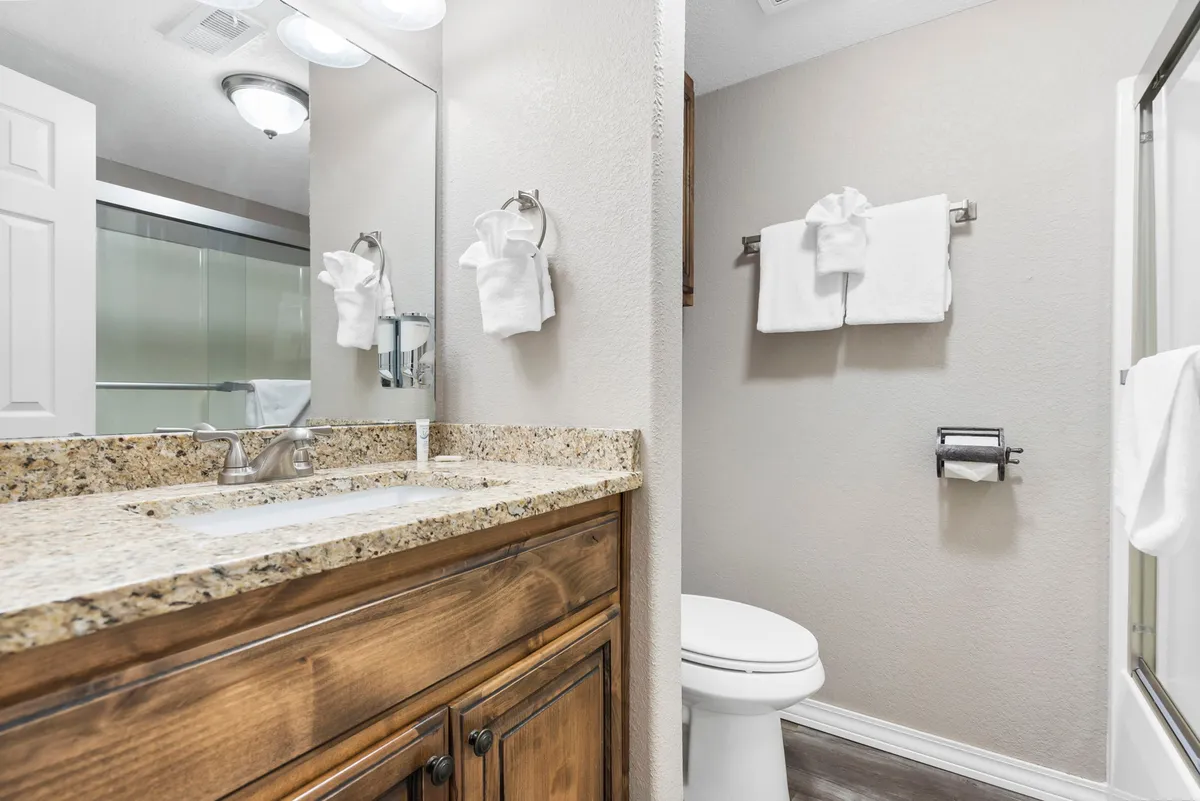 A calming bathroom space with a granite countertop, large mirror, wood cabinetry, and neatly arranged white towels. The atmosphere is fresh and inviting, supporting daily routines and relaxation.