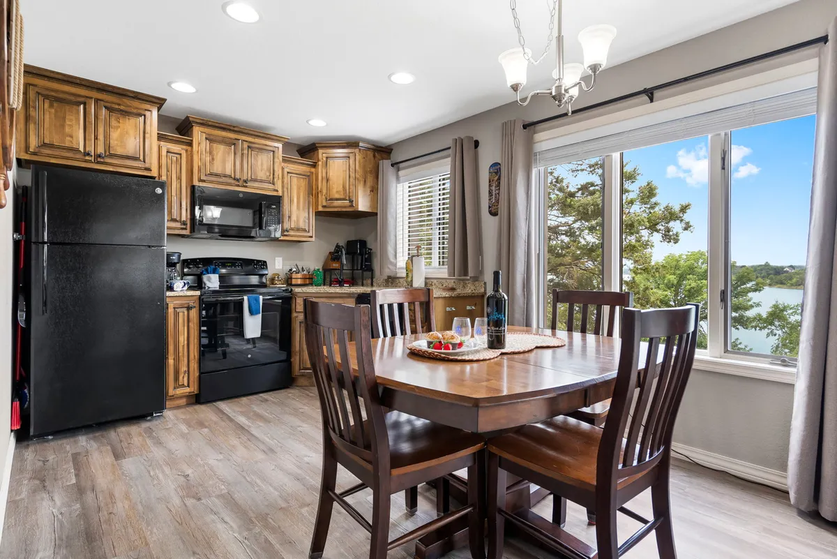 A warm interior shot of a dining area that flows into a kitchen space, with a large dining table, wooden cabinetry, and a window that brings in natural light. The layout feels open and inviting, suitable for family meals or entertaining guests.