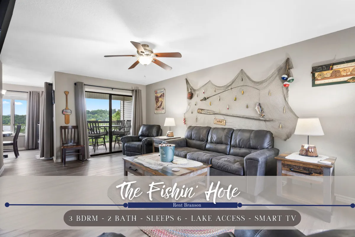 A cozy living room featuring leather sofas arranged around a coffee table, wall decorations, and a large window that offers a view outside. The setting is bright and inviting, perfect for relaxing with family and enjoying entertainment or the scenery.