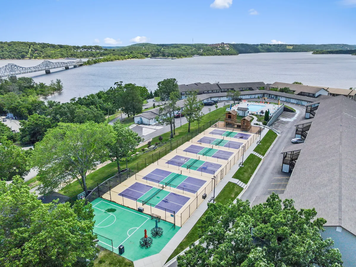 A dynamic exterior shot highlights tennis and basketball courts alongside a swimming pool, all set amidst lush greenery and a waterfront view. Active guests enjoy a variety of sports and poolside play in a vibrant, energetic setting.