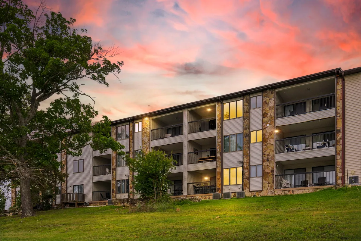Balconies with comfortable seating overlook lush greenery and catch the warm glow of a sunset sky. The stonework and landscaping offer a peaceful, community-oriented outdoor space ideal for relaxing, socializing, or simply taking in the beauty of any season.